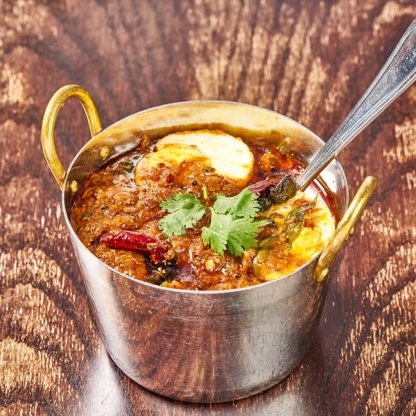 Indian egg curry with cilantro and red chilies in a metal serving bowl with a spoon.