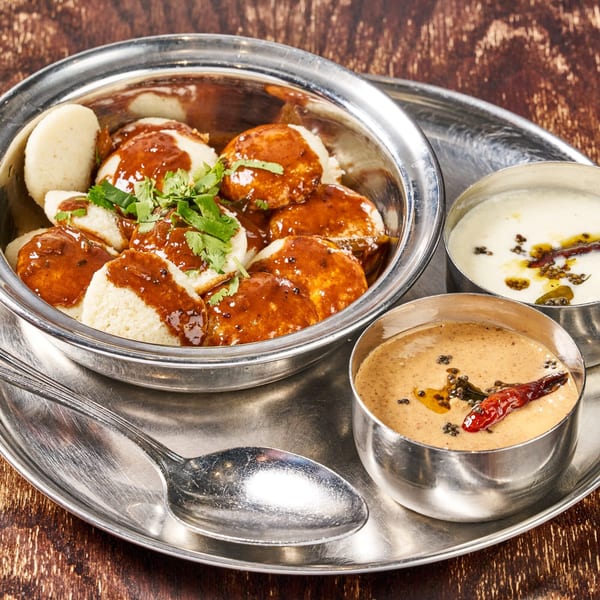 Indian idli with red sauce and cilantro, served with two chutneys on a silver platter.