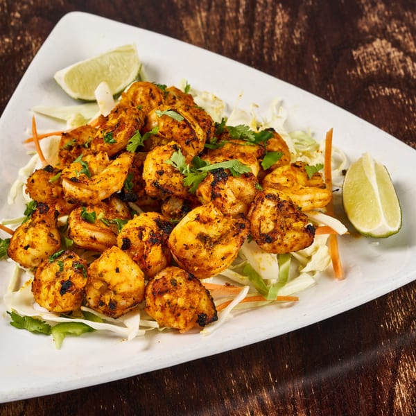 Indian grilled shrimp with cilantro, cabbage, and lime wedges on a white plate.
