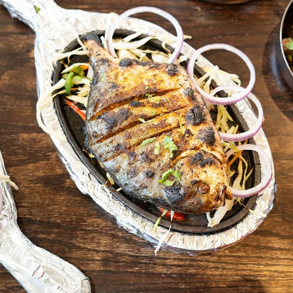 Grilled whole fish, garnished with onions and herbs, served on a sizzling platter.