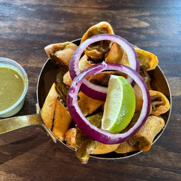 Indian chili pakora with red onion, lime, and green chutney in a brass pan.