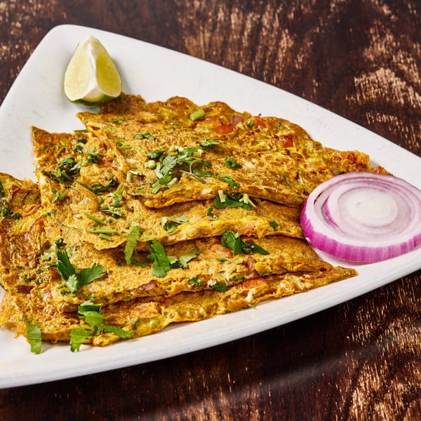 Indian omelets garnished with cilantro, a lime wedge, and a red onion slice on a white plate.