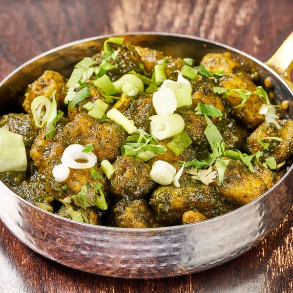 Indian chicken saag in a metal bowl, garnished with fresh cilantro and sliced green onions.