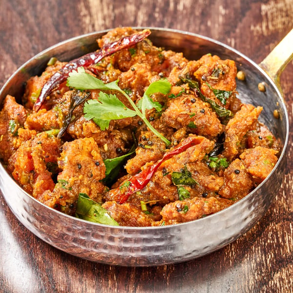 Indian chicken 65, a spicy fried chicken dish, in a hammered metal bowl on a wooden table.