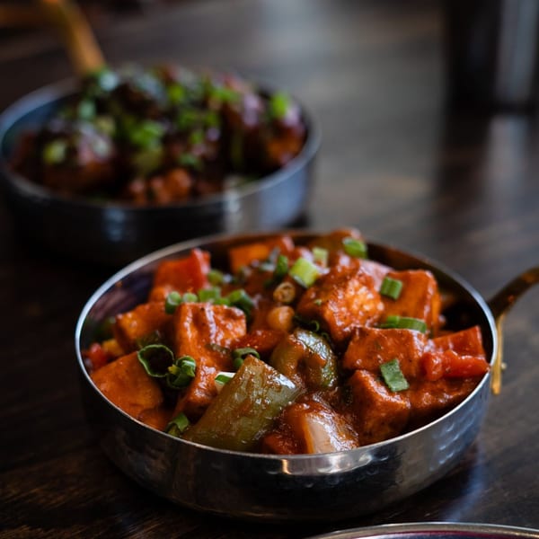 Two bowls of Indian paneer and vegetable curry, garnished with fresh green onions.